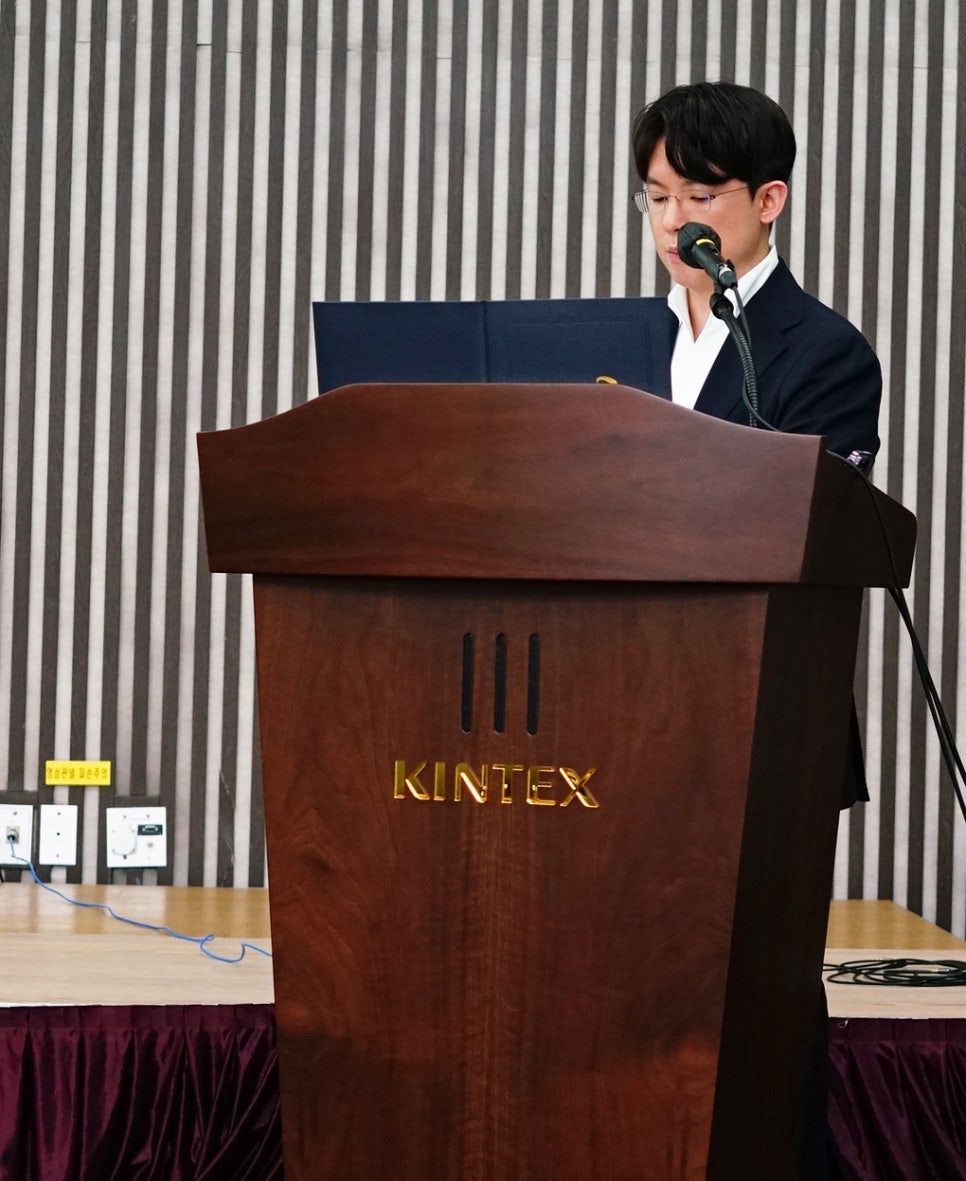 한 남성이 킨텍스 로고가 있는 연단에서 마이크를 잡고 발표하고 있다.