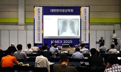 강당에서 강사가 청중에게 흉부 엑스레이 이미지를 보여주며 강의하고 있다.