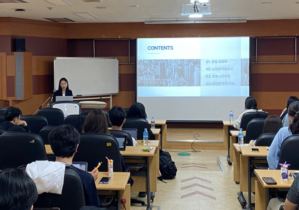 강의실에서 발표자가 화면에 내용을 띄우고 강연하는 모습과 청중들