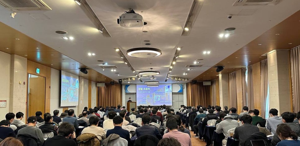 강당에 모인 사람들이 스크린을 보며 강연을 듣고 있다. 스크린에는 정형 초음파 관련 이미지가 표시되어 있다.