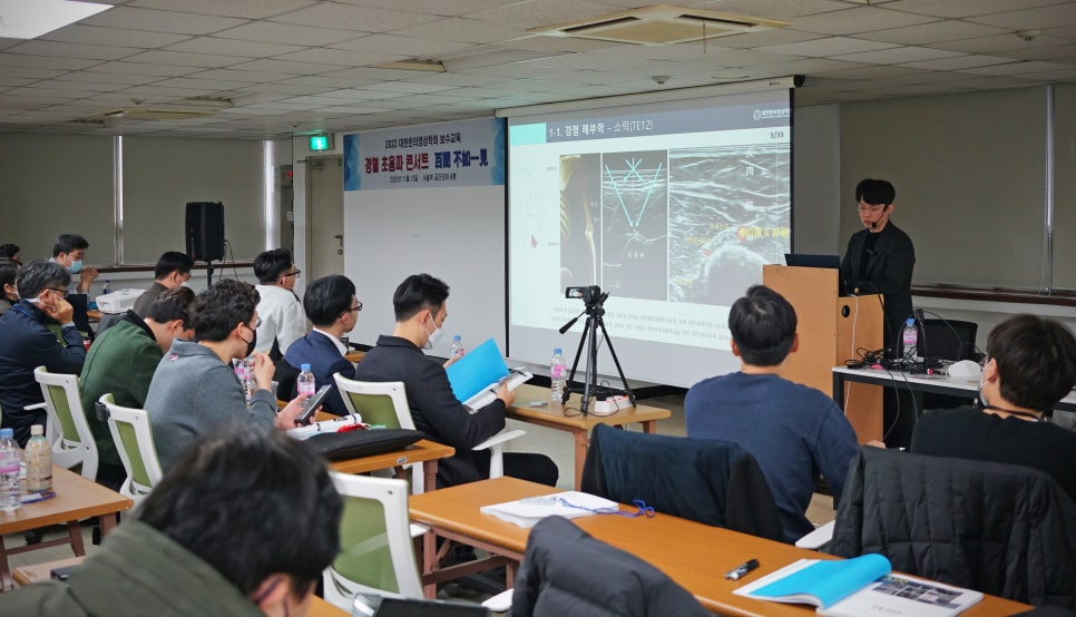 의료 세미나에서 강사가 스크린을 보며 발표하고 참석자들이 앉아서 듣고 있는 모습