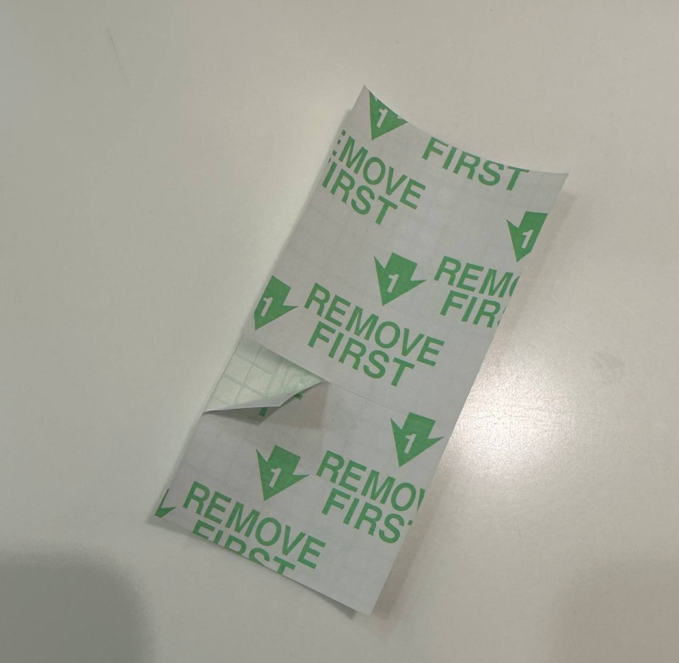 초록색 'REMOVE FIRST' 문구가 인쇄된 흰색 접착 필름의 뒷면이 부분적으로 벗겨져 격자무늬가 보이는 모습 — 초음파 약침·도침 임상 논문 | 서울 바로한의원