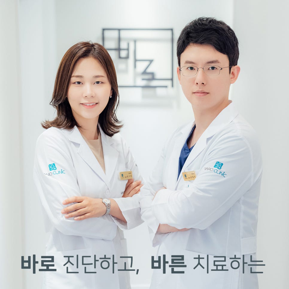 흰색 의사 가운을 입은 남녀 한의사 두 명이 팔짱을 끼고 서서 카메라를 보고 있는 모습.