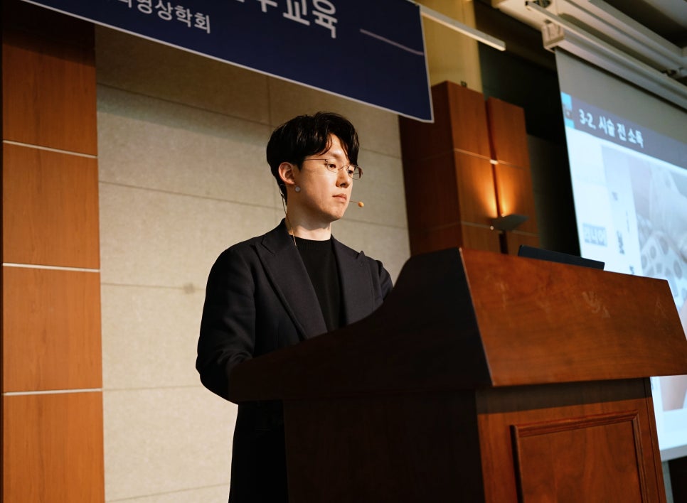 마이크를 착용한 남성이 강단에서 강연하고 있다.