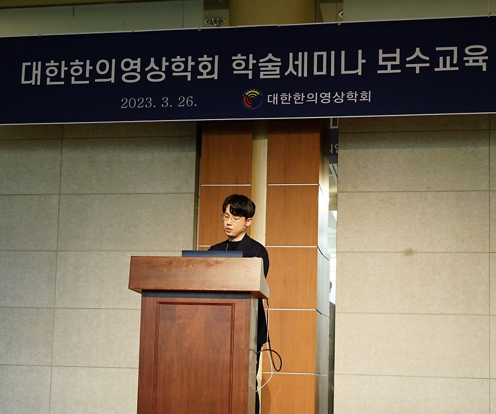 한 남성이 나무 연단에서 발표하고 있으며, 뒤편에는 '대한한의영상학회 학술세미나 보수교육'이라고 적힌 파란색 현수막이 걸려 있다.