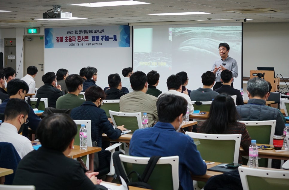 강사가 강당에서 청중에게 초음파 보수교육을 진행하고 있다.