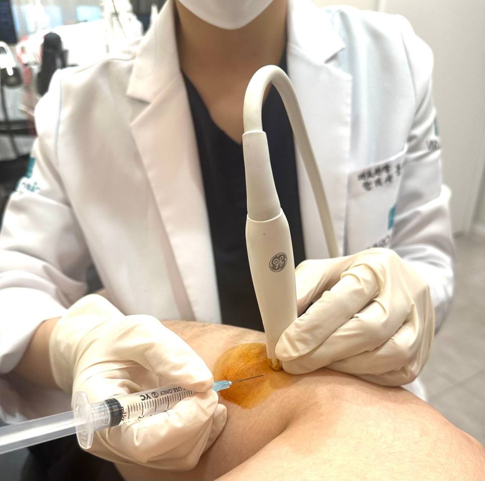 의료진이 환자의 다리에 초음파 유도 주사를 시술하고 있다. 주사 부위는 소독되어 있다.