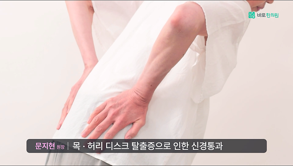 흰 상의를 입은 사람이 허리를 숙인 채 양손으로 허리를 짚고 있는 뒷모습.