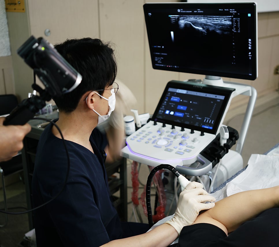 마스크를 착용한 의료진이 환자의 팔에 초음파 탐촉자를 대고 초음파 검사를 진행하는 모습