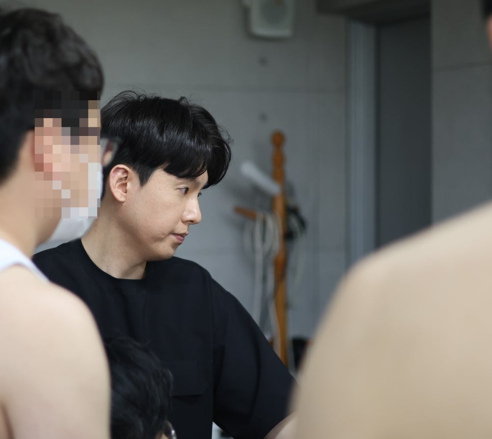 검은색 상의를 입은 남성이 다른 사람들과 함께 아래를 내려다보고 있는 모습