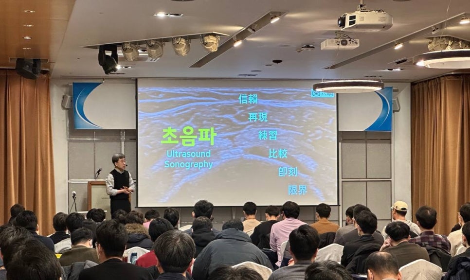 강사가 강단에서 초음파 관련 내용을 대형 스크린에 띄워놓고 청중에게 설명하고 있는 모습