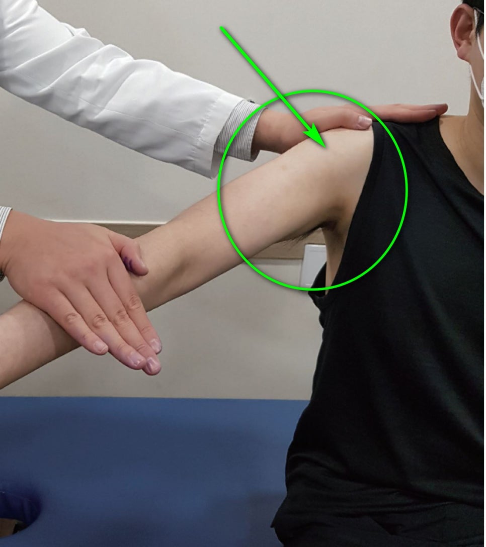 한의사가 환자의 어깨를 진찰하며 초록색 원과 화살표가 어깨 부위를 가리키고 있는 모습.