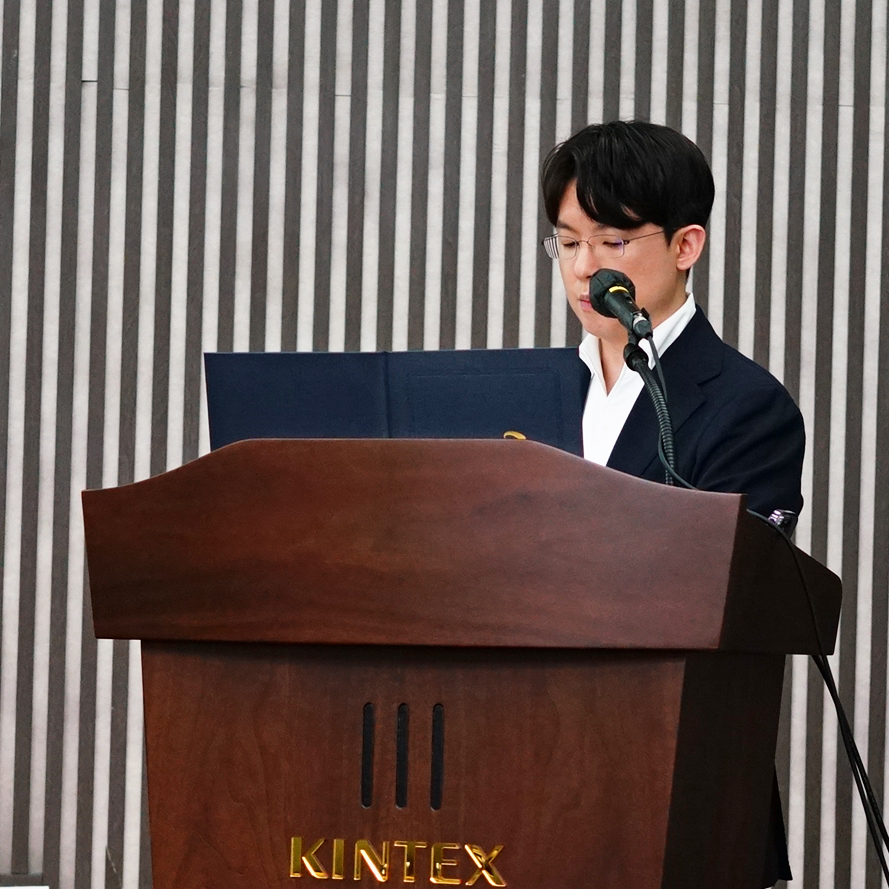 안경을 쓴 남성이 마이크가 있는 나무 연단에서 강연하고 있다.