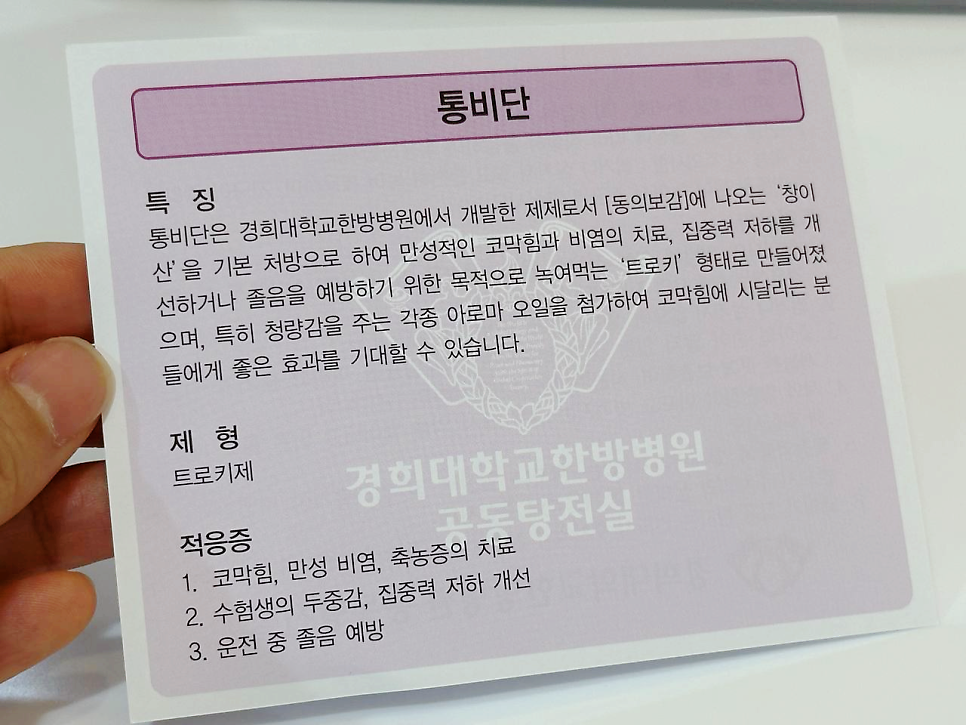 손이 통비단 제품의 특징, 제형, 적응증이 적힌 안내문을 들고 있는 모습.