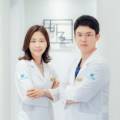 흰색 의사 가운을 입은 남성과 여성이 팔짱을 끼고 서 있는 모습