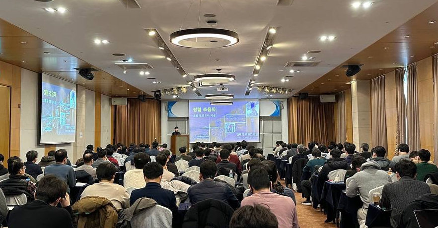 강의실에서 많은 사람들이 앉아 강연을 듣고 있다. 강단 뒤 스크린에는 '경혈 초음파'라는 제목과 초음파 영상이 보인다.