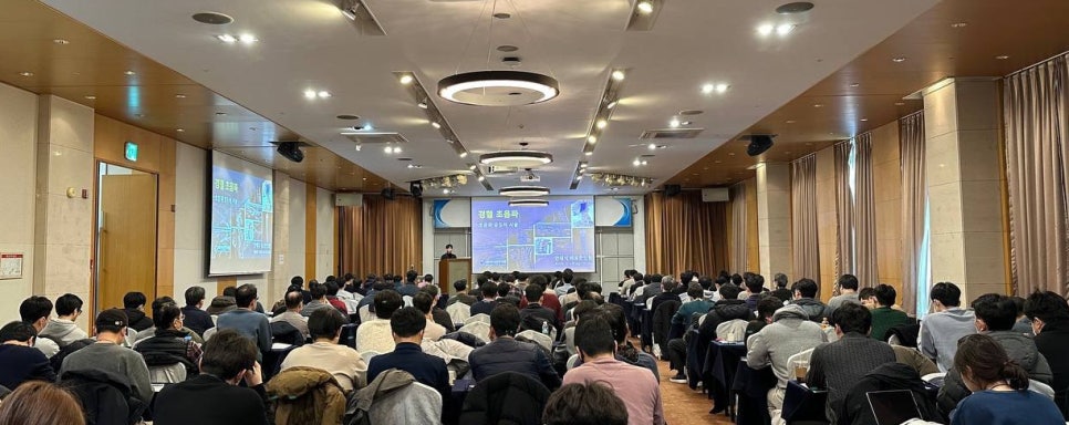 강당에서 많은 사람들이 강연을 듣고 있으며, 스크린에는 '정밀 초음파'라는 글자가 보인다.