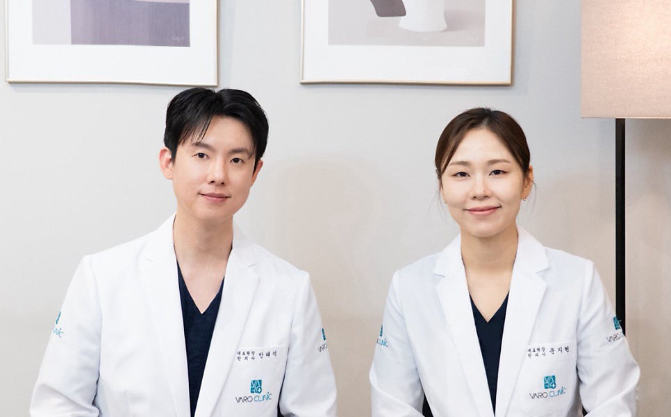 흰색 가운을 입은 두 명의 한의사가 카메라를 보며 미소 짓고 있다.