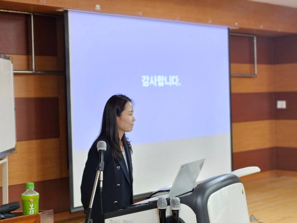 강단에서 마이크 앞에 서서 발표하는 여성의 모습. 뒤쪽 스크린에는 '감사합니다'라는 문구가 보인다.
