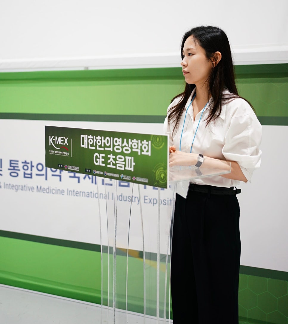 한의영상의학회 GE 초음파라고 적힌 연단 옆에 서 있는 여성