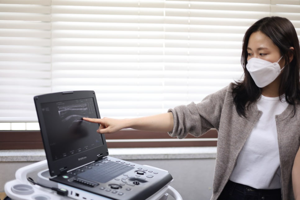마스크를 쓴 여성이 초음파 기기 화면을 손가락으로 가리키고 있다.