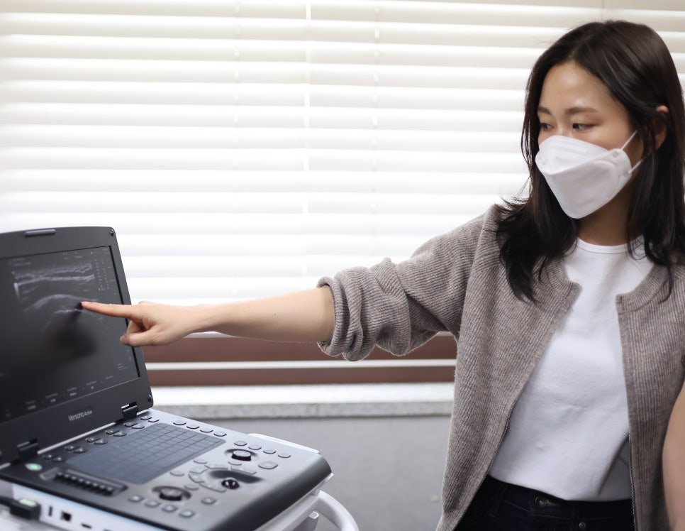 마스크를 쓴 여성이 초음파 화면을 가리키고 있다.