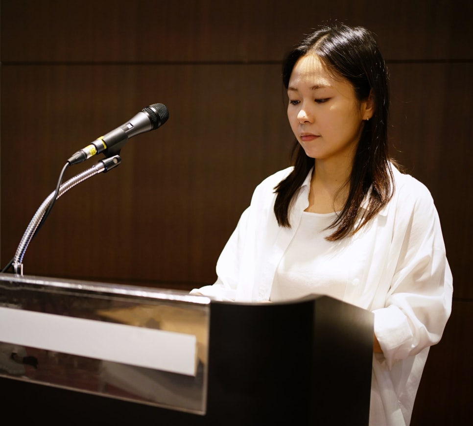 마이크가 있는 연단에 서서 아래를 보고 있는 여성